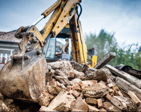 A bulldozer is clearing rubble in front of a house, preparing the site for construction or renovation work.