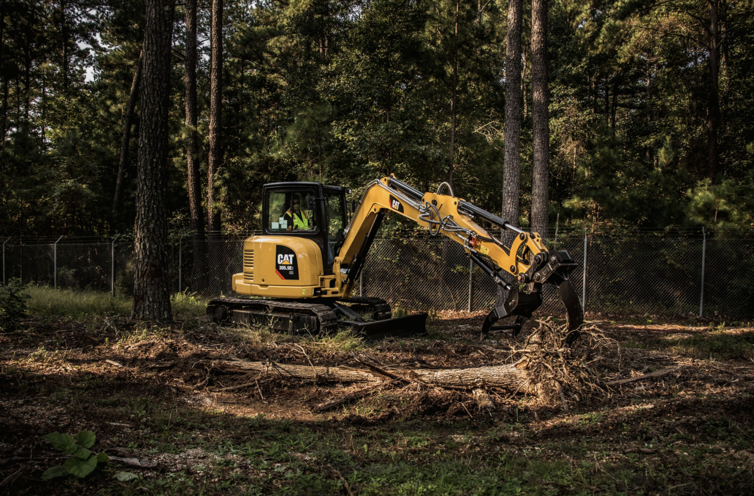 A yellow excavator digging in a wooded area, surrounded by trees and earth being displaced.