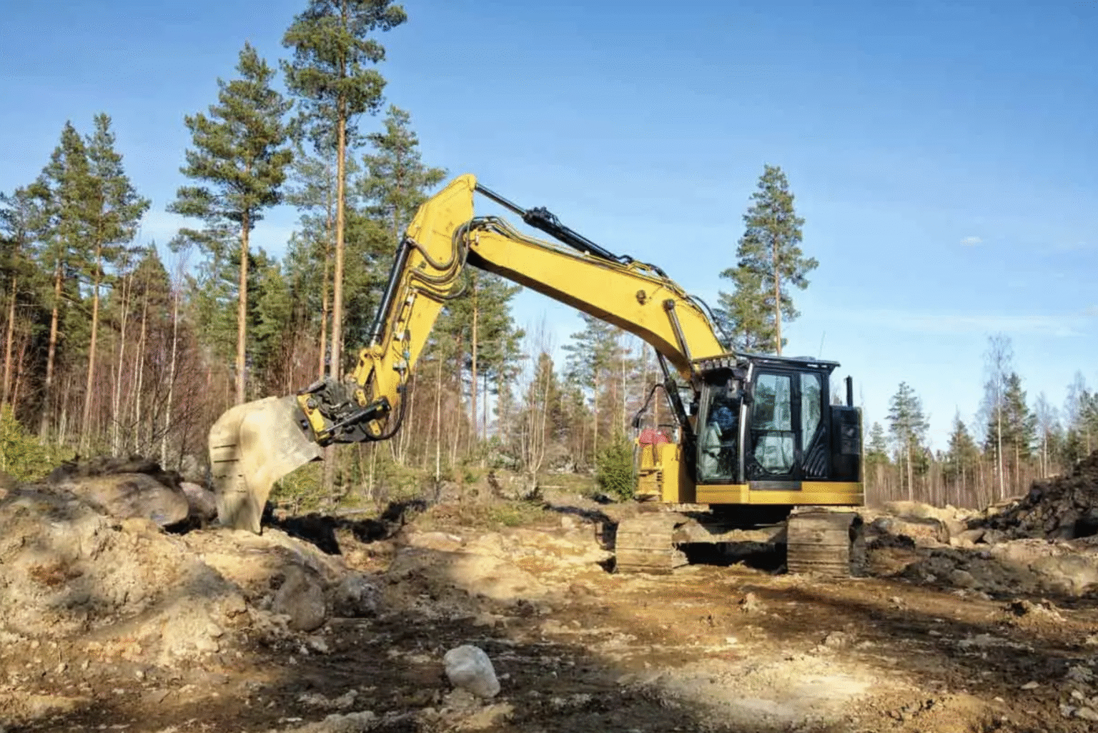 A yellow excavator is actively digging on a dirt road, surrounded by piles of earth and construction materials.